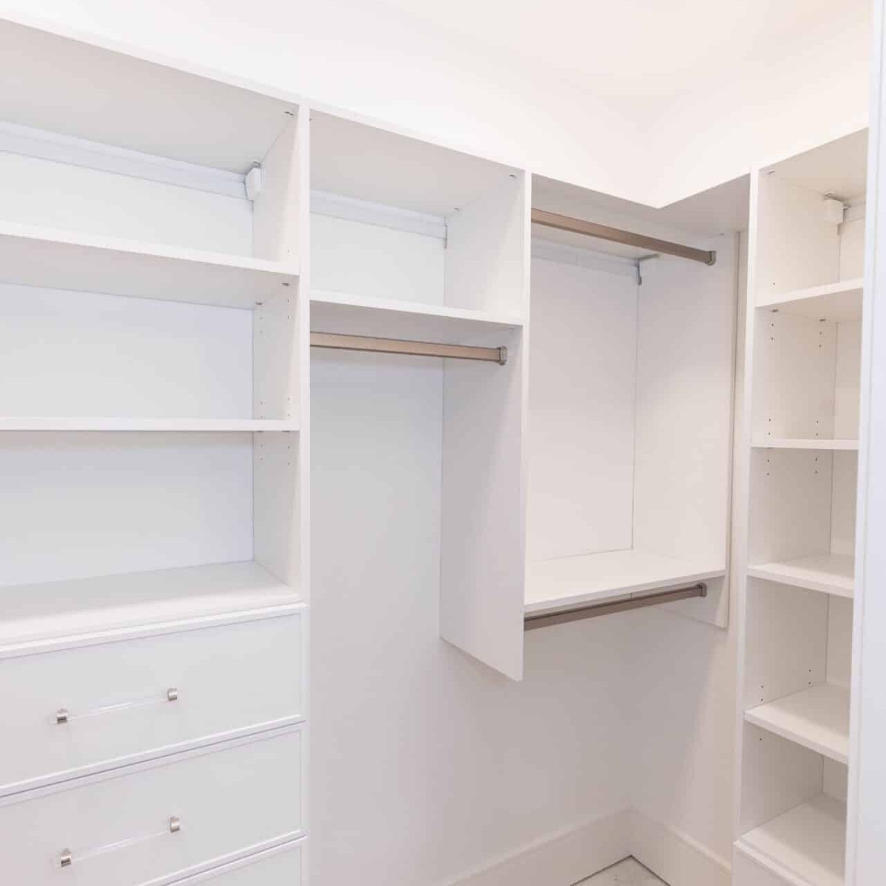 White corner walk-in closet with double hang rods and drawer bank